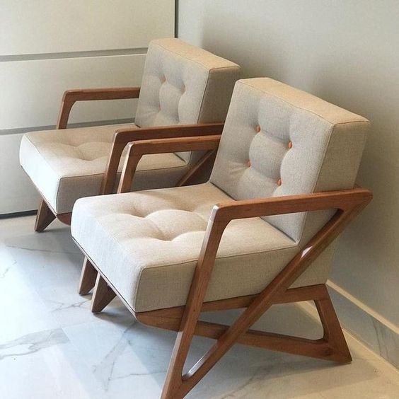 Dos modernos sillones beige con estructura de madera están colocados uno al lado del otro sobre un suelo de mármol.